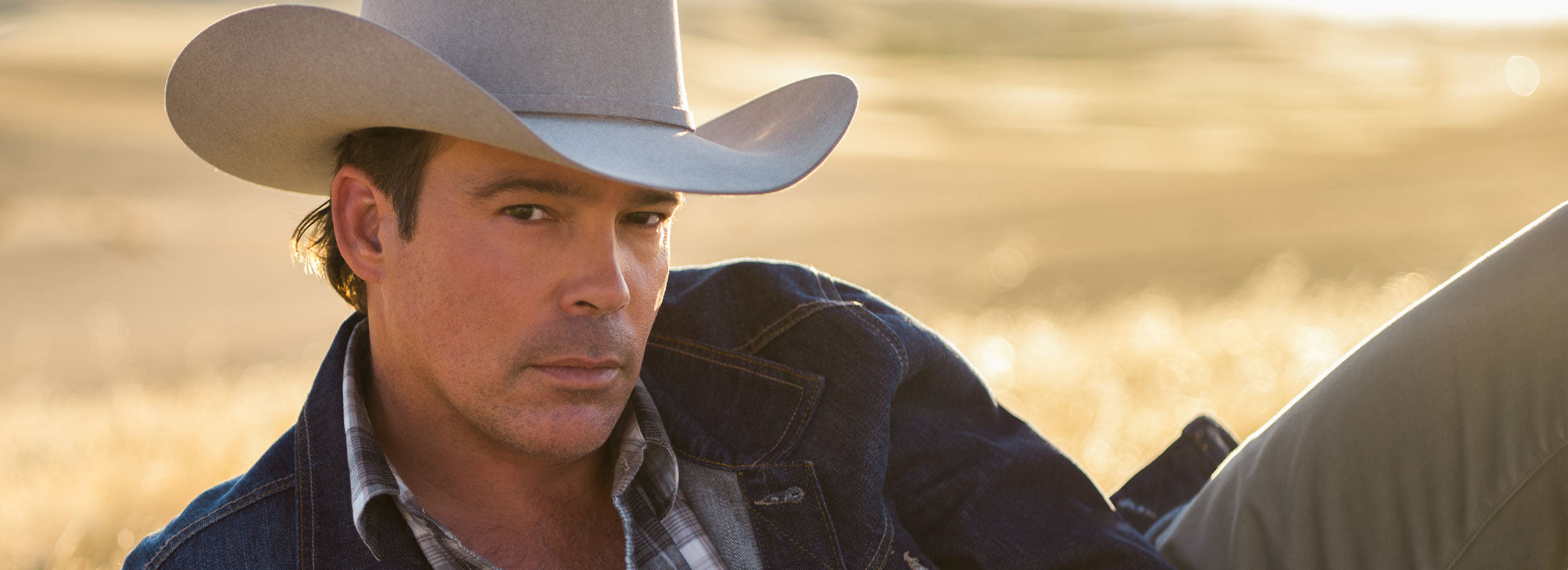 Photo of Clay Walker laying in a field wearing a denim jacket