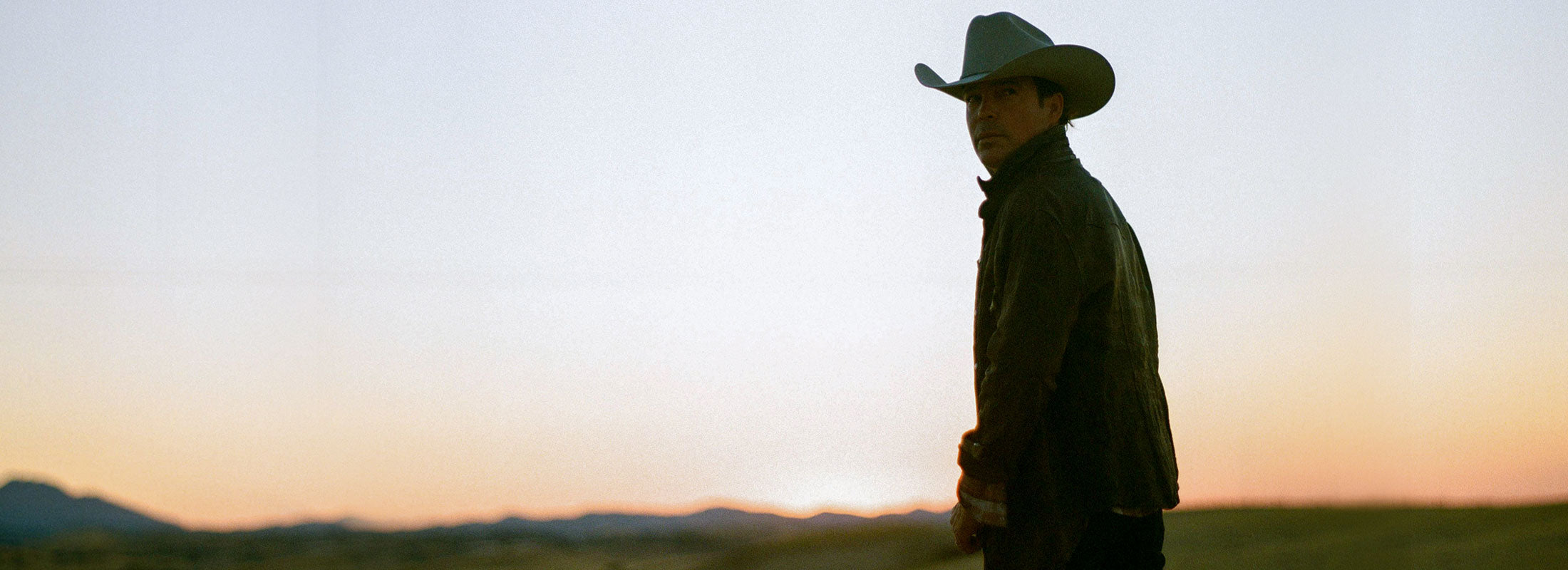 Clay Walker looking over his shoulder in a cowboy hat with a sunset in the background