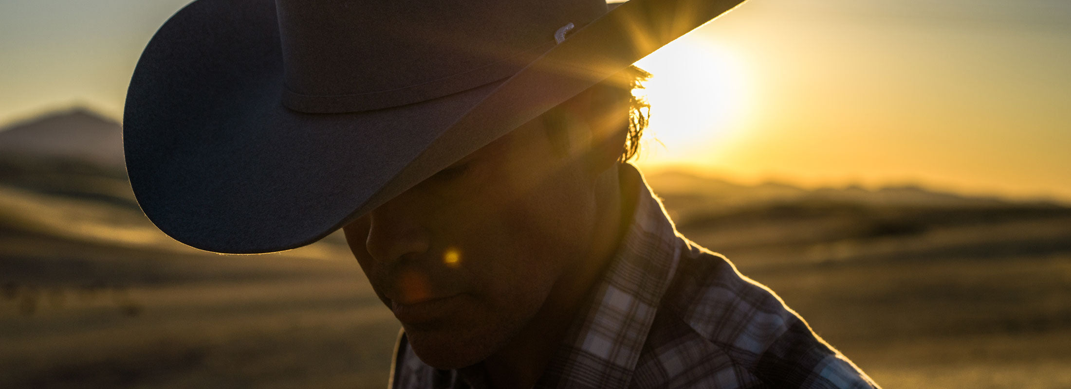 Clay Walker in a cowboy hat looking down while the sun sets in the background